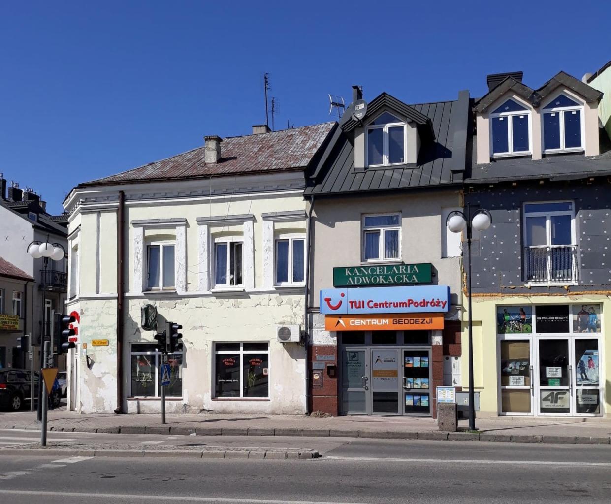 Budynek z szyldem 'Centrum Geodezji' pod szyldami 'Kancelaria Adwokacka' i 'TUI Centrum Podróży', widok z ulicy w słoneczny dzień.