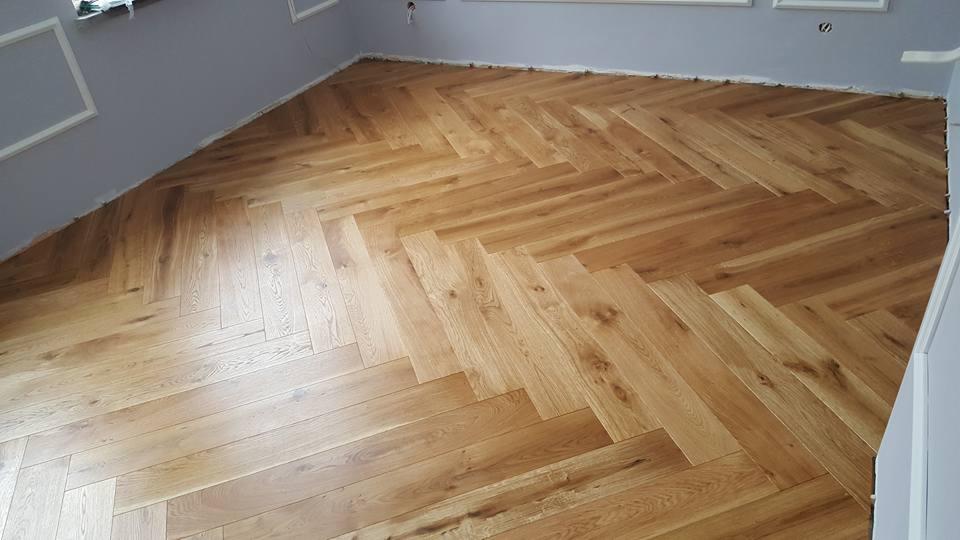 Ułożona w jodełkę jasna drewniana podłoga w Słupsku, widoczne listwy przypodłogowe w trakcie montażu.