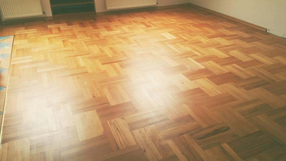 Parkiet ułożony w jodełkę po renowacji, widoczne odświeżone drewno i brak śladów zużycia, delikatne refleksy światła podkreślają gładką powierzchnię.