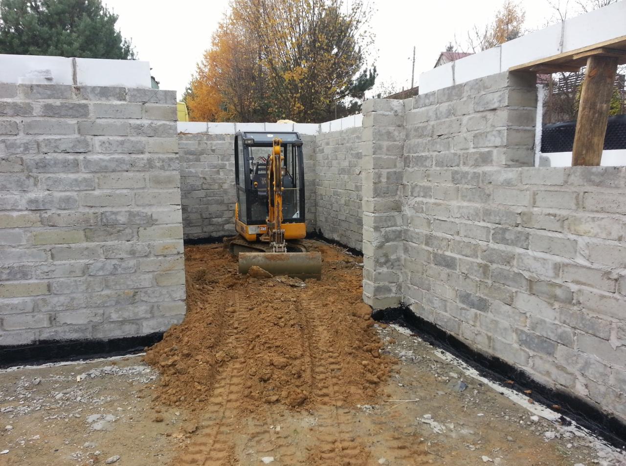 Mini koparka wewnątrz fundamentów z bloczków betonowych, zabezpieczonych czarną izolacją, Częstochowa.