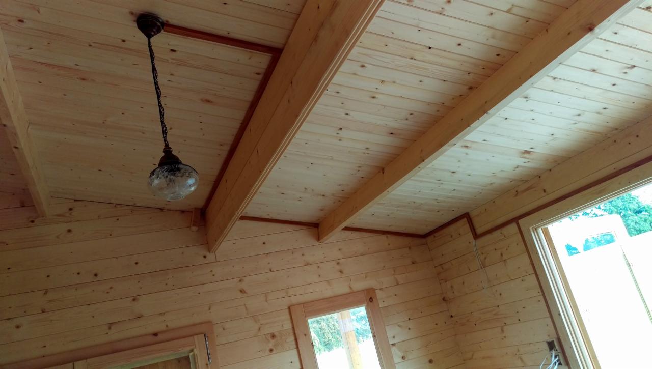 Drewniany sufit z widocznymi belkami i wiszącą lampą w stylu retro z kloszem z wzorzystego szkła.