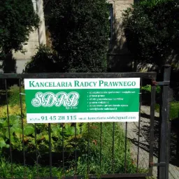 Tablica informacyjna Kancelarii Radcy Prawnego SDRB Sp. z o.o. umieszczona na metalowym ogrodzeniu, z wykazem oferowanych usług prawnych i danymi kontaktowymi, otoczona zielenią.