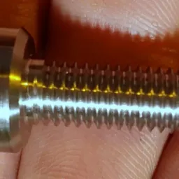 Metalowy śruba z gwintem, trzymana w palcach, ukazująca precyzję wykonania i detale obróbki.