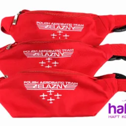 Stos czerwonych saszetek-nerek z białym nadrukiem 'Polish Aerobatic Team Żelazny' oraz logo firmy Haftoria, prezentowane na białym tle.