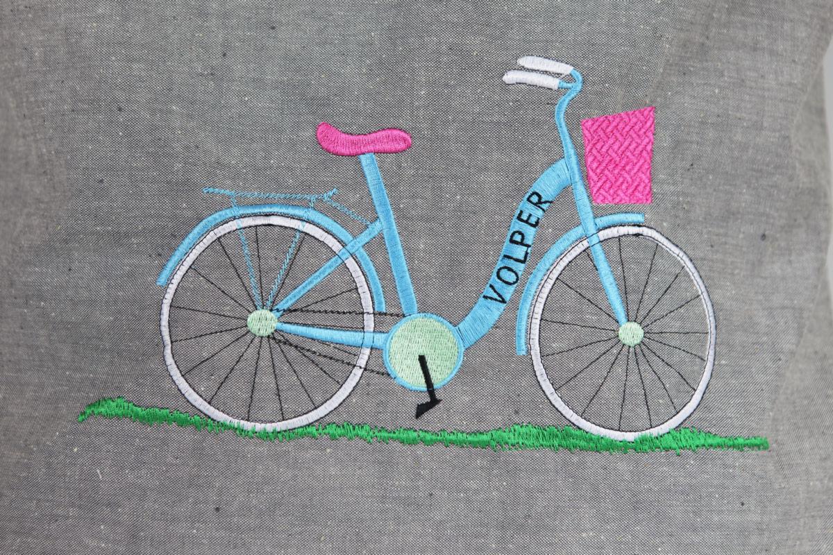 Szary materiał z wyhaftowanym wzorem roweru w pastelowych kolorach (błękit, róż, zieleń) i napisem 'VOLPER' na ramie.