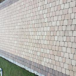 Techmax - Ułożona kostka brukowa w odcieniach beżu i brązu, obrzeże z ciemniejszej kostki i kamieni, widoczny fragment trawnika i rury PCV.