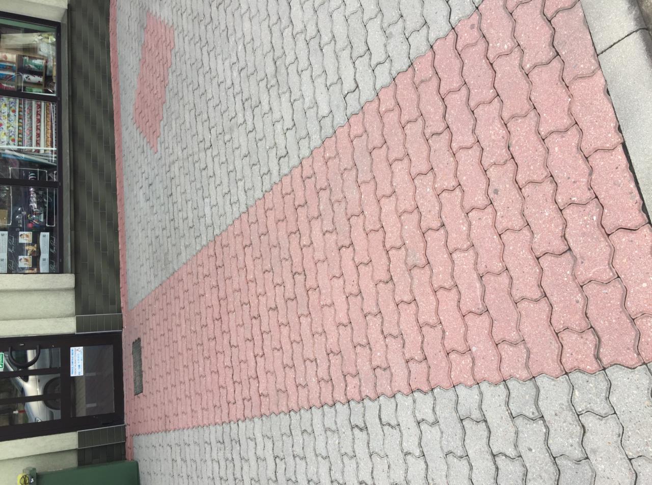Ułożona kostka brukowa w kolorze szarym i różowym przed wejściem do budynku z przeszklonymi drzwiami i oknami wystawowymi.