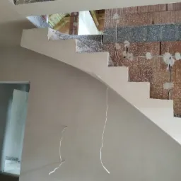 Tynki maszynowe na ścianie i schodach w surowym stanie, widoczne przewody elektryczne wystające ze ściany z cegły dziurawki.