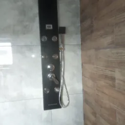 Nowoczesna kabina prysznicowa z panelem natryskowym w kolorze czarnym, zamontowana na tle szarych płytek imitujących beton, z widoczną ścianą wyłożoną płytkami drewnopodobnymi.