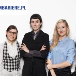 Grupa pięciu os&oacute;b w r&oacute;żnym wieku, ubranych w formalne stroje, stojących na tle białej ściany, z widocznym logo firmy 'Przelambariere.pl' w g&oacute;rnej części zdjęcia.