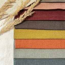 Próbki tkanin w różnych kolorach ułożone warstwowo, z dekoracyjnym suszem w rogu, prezentacja palety barw.