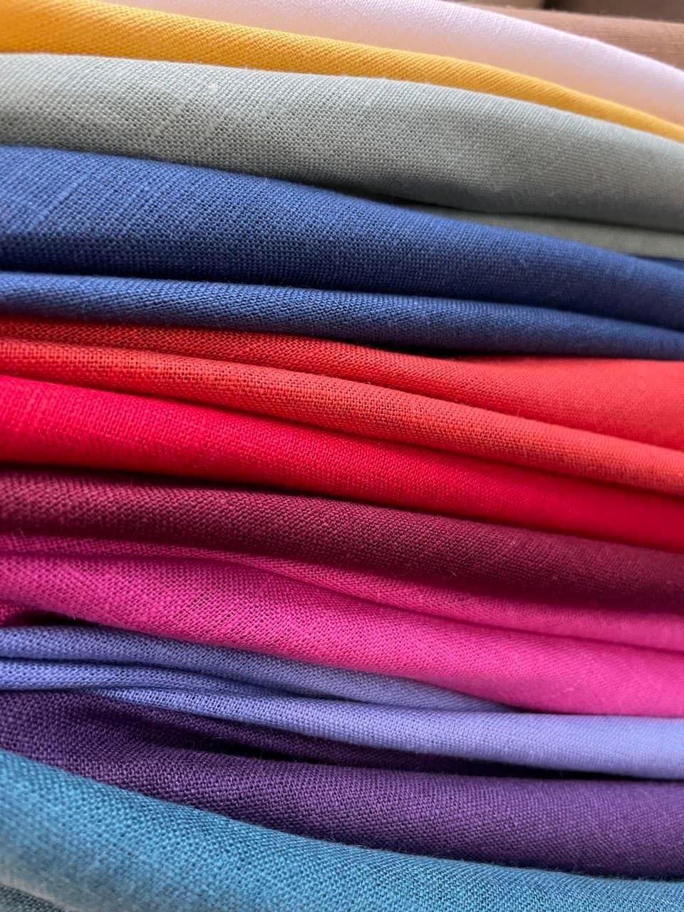 Stos różnokolorowych tkanin bawełnianych w Łodzi, ułożonych warstwami od żółtego po turkusowy, prezentujący fakturę materiałów.