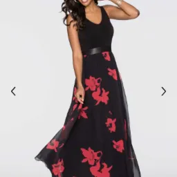 Uśmiechnięta kobieta w zwiewnej, czarnej sukience maxi z czerwonymi kwiatami, prezentowana przez firmę z Lyski. Sukienka ma czarny top na ramiączkach i cienki pasek w talii.