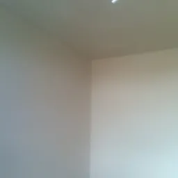 Wnętrze pokoju po nałożeniu tynków gipsowych; widoczne gładkie, jasne ściany i sufit w rogu pomieszczenia, z wystającym przewodem elektrycznym.