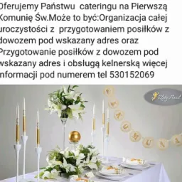 Dekoracja stołu komunijnego z białymi liliami, złotymi świecami i napisem 'Komunia' na girlandzie, widoczne talerze z dekoracjami, logo firmy w prawym górnym rogu.