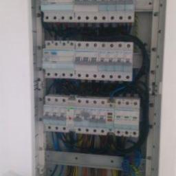 el4you - Otwarta skrzynka bezpiecznikowa z zainstalowanymi wyłącznikami różnicowoprądowymi i nadprądowymi, widoczne liczne przewody w różnych kolorach, zwój czarnego kabla u dołu.