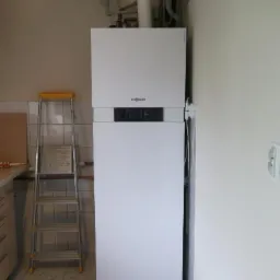 Biały, kondensacyjny piec gazowy Viessmann zamontowany przy ścianie, widoczne rury i zbiornik wyrównawczy, obok drabina aluminiowa.