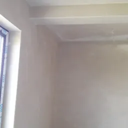 Wnętrze pokoju po nałożeniu świeżej, jasnej warstwy gładzi szpachlowej na ścianach i suficie, widoczne delikatne nierówności i ślady po narzędziach, okno po lewej stronie kadru.