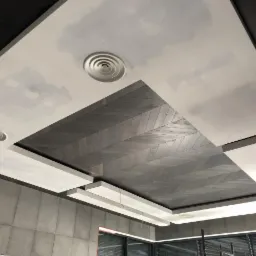 Sufit z fragmentem wykończonym drewnem ułożonym we wzór jodełki, obok fragmenty sufitu z widocznymi śladami po szpachlowaniu, kratki wentylacyjne oraz oświetlenie ledowe.