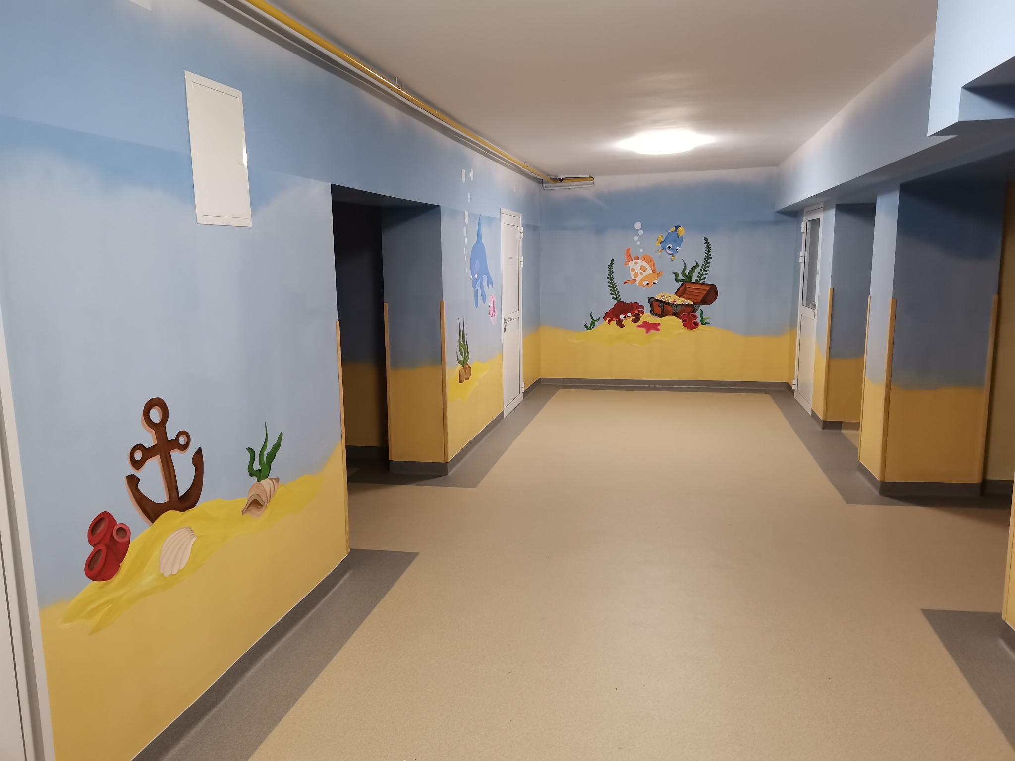 Korytarz z motywami morskimi: malowidła przedstawiające dno morza z kotwicą, muszlami, rybami i skrzynią skarbów na ścianach pomalowanych w odcieniach błękitu i piasku.
