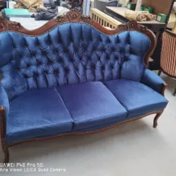 Odnowiona, trzyosobowa sofa w stylu vintage z ciemnoniebieską, aksamitną tapicerką i drewnianą ramą z dekoracyjnymi rzeźbieniami, widoczne detale nitowania tapicerskiego.