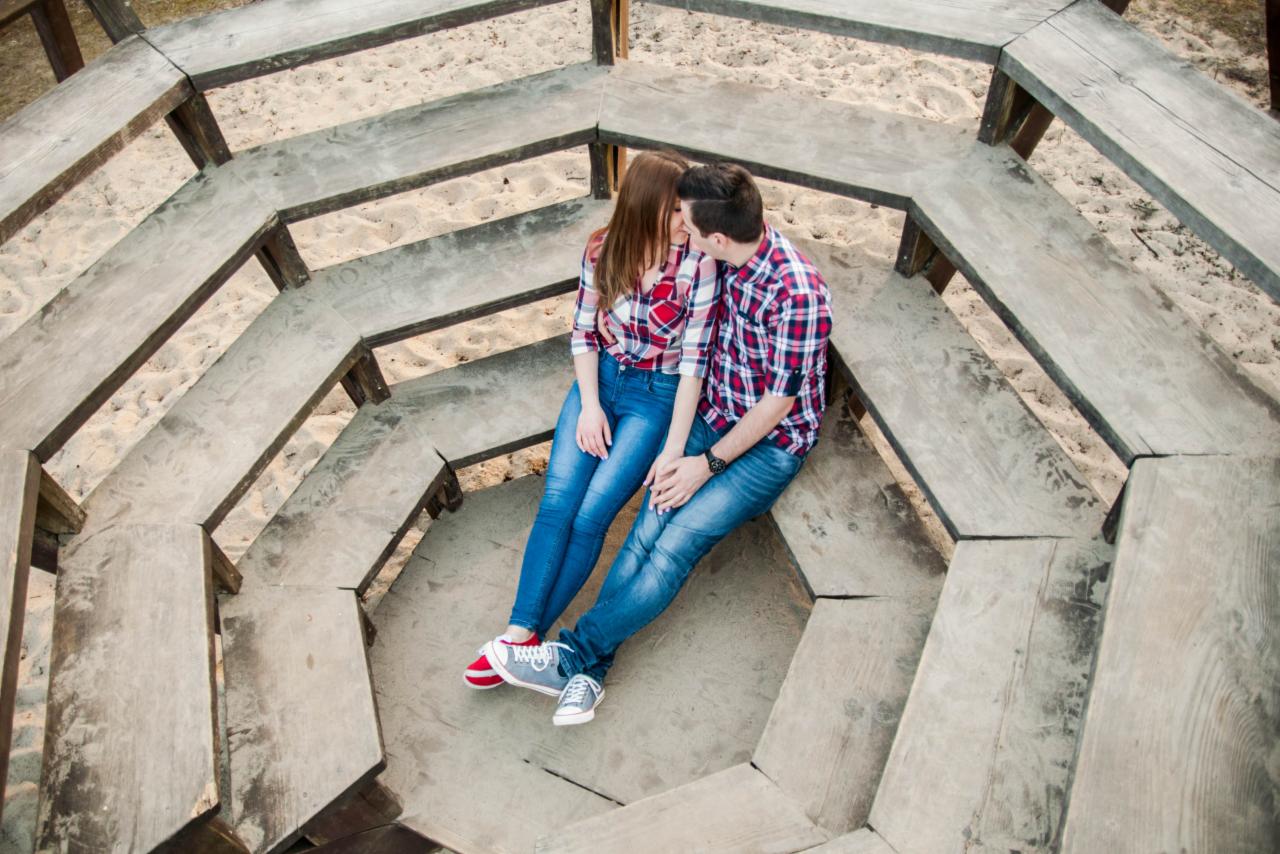 Zakochana para w czerwono-niebieskich koszulach w kratę siedzi na drewnianych schodach w kształcie oktagonu i całuje się.