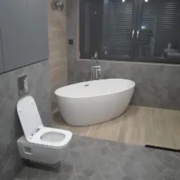 Nowoczesna łazienka z wolnostojącą wanną, podwieszaną toaletą z otwartą deską, szarą geometryczną glazurą i drewnopodobną podłogą w strefie prysznica.