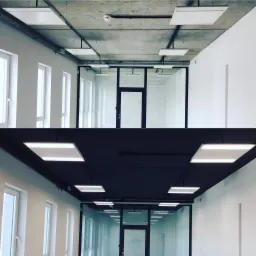 Zdjęcie przedstawia korytarz biurowy w Bydgoszczy, podzielony na dwie części: górna z surowym, betonowym sufitem i białą ścianą, dolna z ciemnym, pomalowanym sufitem i białą ścianą. Widoczne są...