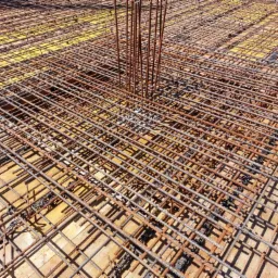 Siatka zbrojeniowa na deskowaniu z widocznymi dystansami z tworzywa i pionowymi prętami zbrojeniowymi, przygotowana do wylewki betonowej.