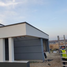 Henryk Łęgowski - Wykończony budynek z obróbkami blacharskimi, widoczny pracownik z drabiną i otwarty bagażnik samochodu w tle.