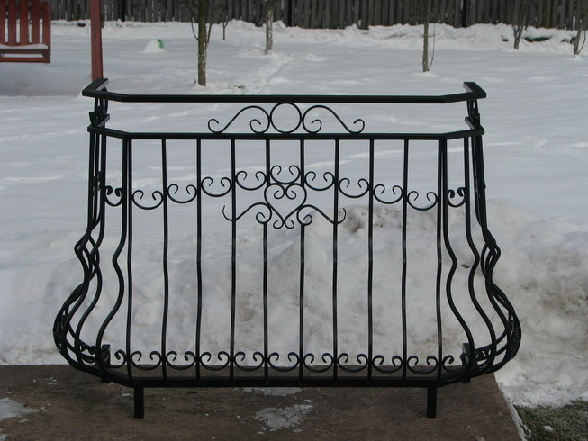 Kuta, czarna balustrada balkonowa z dekoracyjnymi elementami w kształcie serc i spirali na tle zaśnieżonego ogrodu.