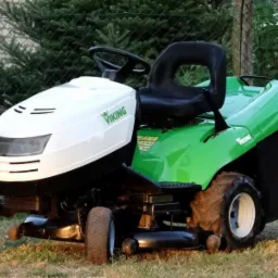 Zielono-biała kosiarka traktorowa marki Viking, stojąca na trawie przed żywopłotem i ogrodzeniem z siatki.