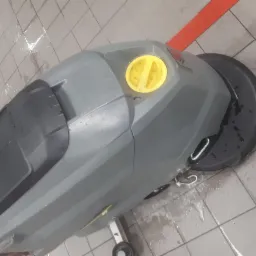 Szorowarka automatyczna do podłóg na mokrych, szarych płytkach w Górkach Wielkich, z widoczną czerwoną linią na podłodze w tle.