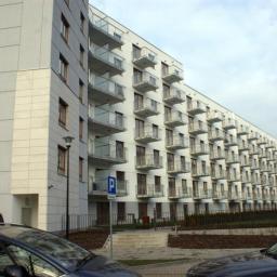 Inwest-Profil Sp.Z O. O. Sp. k. - Nowoczesny budynek wielorodzinny z białymi elewacjami i balkonami z przeszklonymi balustradami, widok z poziomu ulicy z zaparkowanymi samochodami.