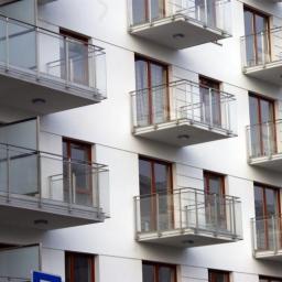 Inwest-Profil Sp.Z O. O. Sp. k. - Nowoczesny budynek z białymi ścianami i balkonami z przeszklonymi balustradami, widoczne brązowe ramy okienne.