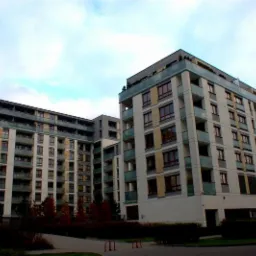 Nowoczesny kompleks apartamentowy z balkonami i oknami, widok z poziomu ulicy w pochmurny dzień.