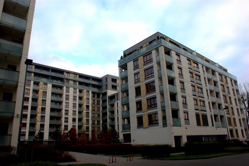 Nowoczesny kompleks apartamentowy z balkonami i oknami, widok z poziomu ulicy w pochmurny dzień.