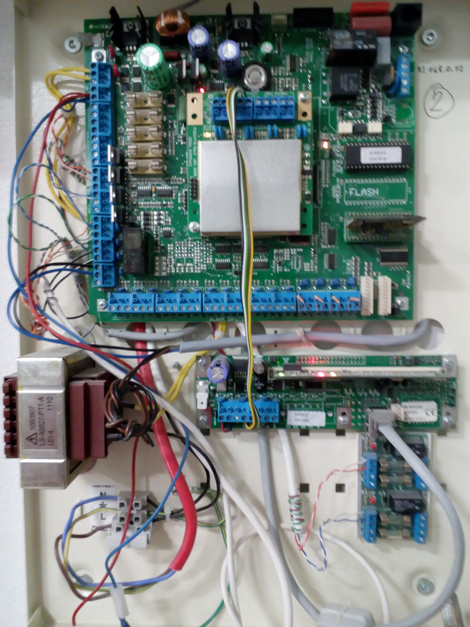 Panel sterowania z elektroniką, widoczne liczne kable, złącza, transformator i układy scalone wewnątrz białej obudowy.