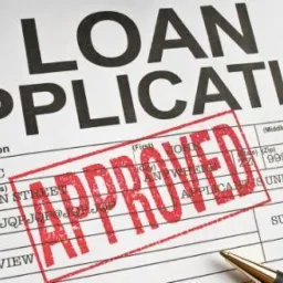 Wypełniony formularz wniosku o pożyczkę z odciśniętą czerwoną pieczątką 'APPROVED' i leżącym obok długopisem.