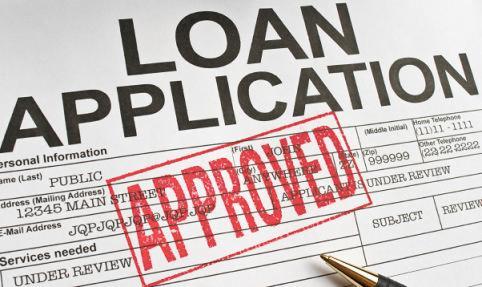 Wypełniony formularz wniosku o pożyczkę z odciśniętą czerwoną pieczątką 'APPROVED' i leżącym obok długopisem.