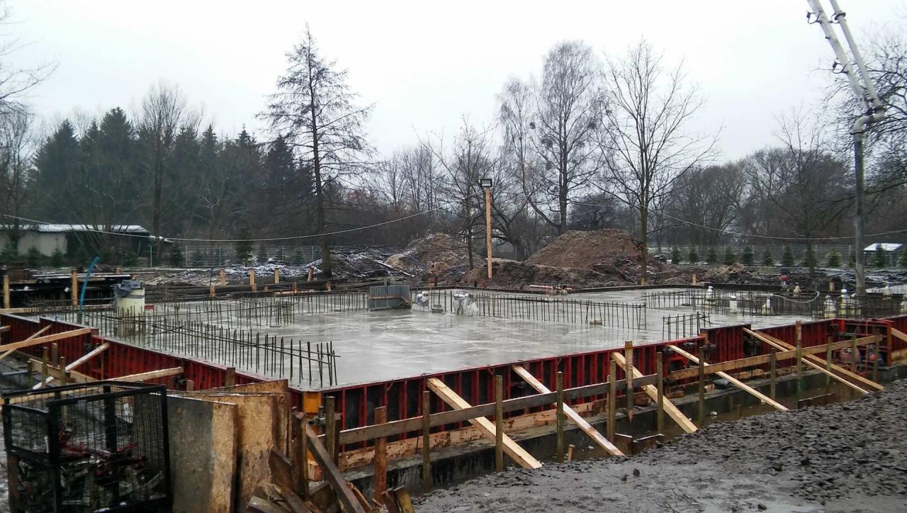 Wylany fundament domu jednorodzinnego zbrojony stalą, widoczne szalunki i przygotowany teren budowy w pochmurny dzień.