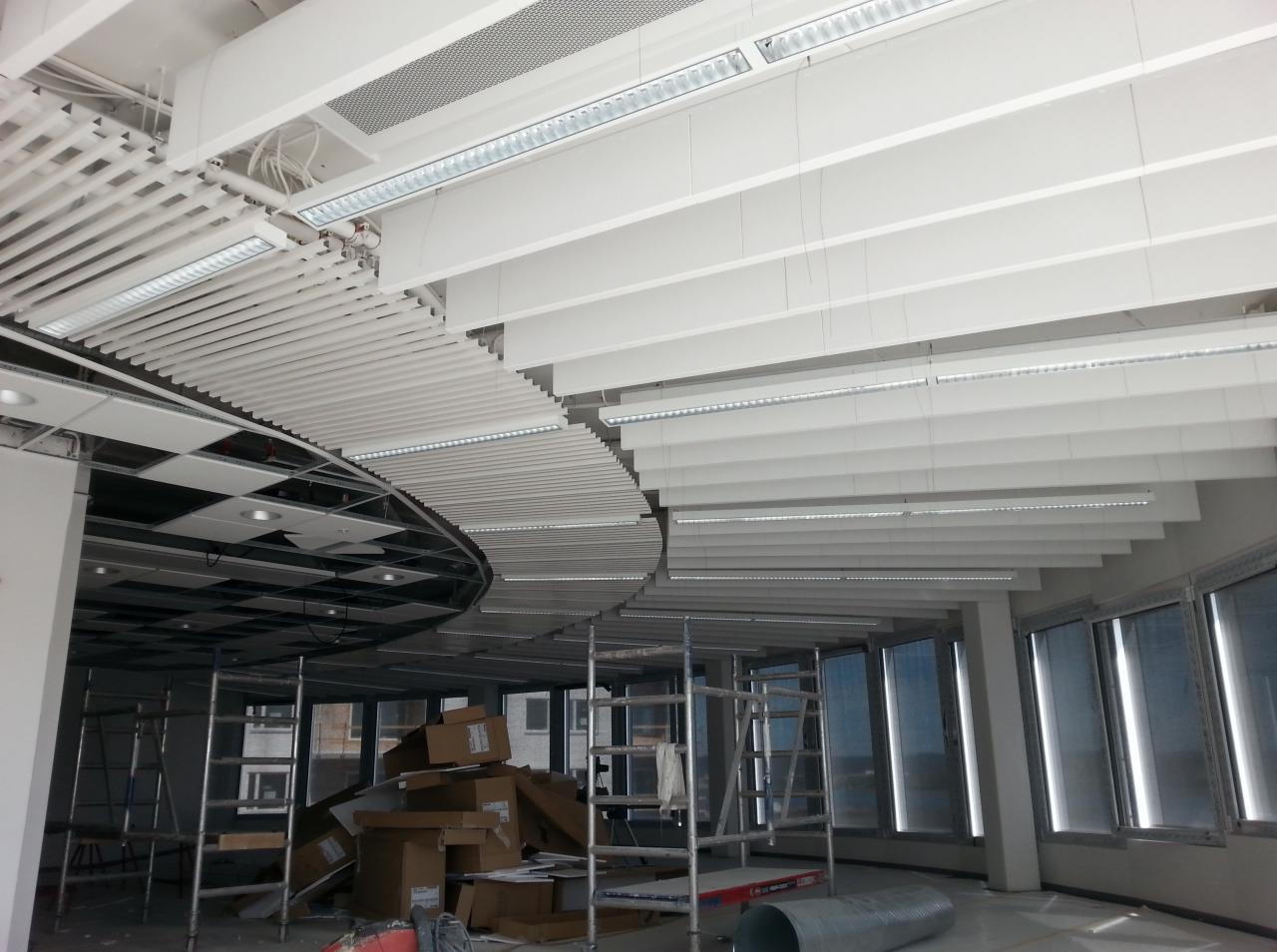 Montaż sufitu podwieszanego z oświetleniem LED w nowoczesnym biurze, widoczne rusztowania i materiały budowlane.