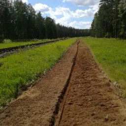 Przygotowany pas ziemi z wykopanym rowkiem, prawdopodobnie pod sadzenie drzew, widok w kierunku oddalającego się lasu, obok torów kolejowych.