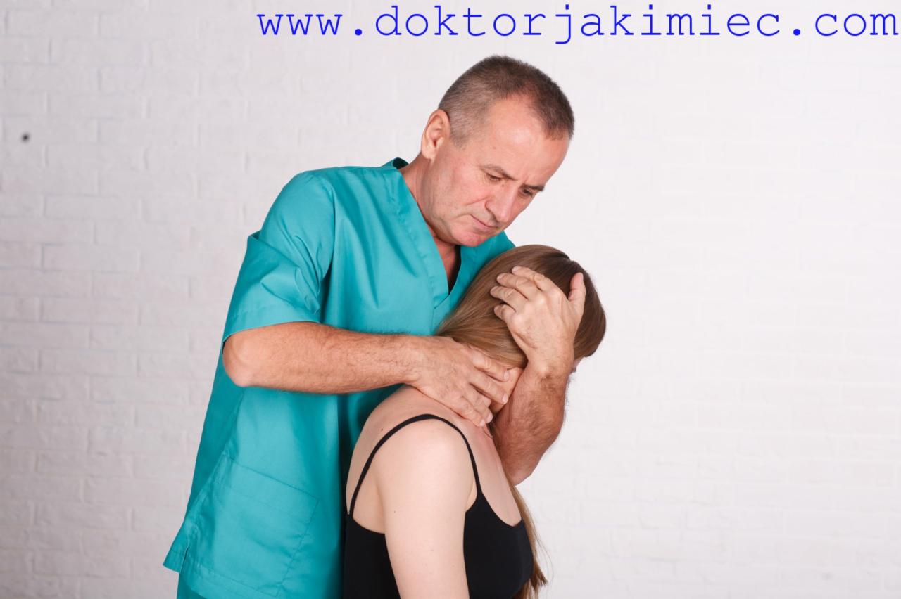 Mężczyzna w turkusowym uniformie uciska kark pacjentki podczas sesji terapeutycznej na tle białej ściany z cegieł. Widoczny adres strony internetowej w górnej części kadru.
