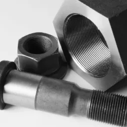 Precyzyjnie obrobiony metalowy trzpień z gwintem, nakrętka i sześciokątny element z gwintowanym otworem, leżące na białym tle, ukazujące dokładność wykonania.