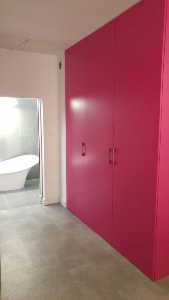 Różowa szafa wnękowa z czterema drzwiami i srebrnymi uchwytami w łazience z wanną wolnostojącą i szarymi płytkami.