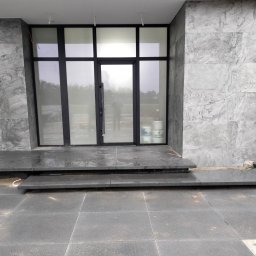 Bruk-Tim - Nowoczesne wejście do domu z szarej kostki granitowej. Schody i podest wyłożone gładkimi płytami, ściany obłożone marmurem. Minimalistyczny design, surowe wykończenie.