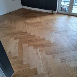 Ułożony parkiet w jodełkę w Wiśniowej, widoczne przygotowane ściany do malowania i drzwi balkonowe. Podłoga z jasnego drewna.