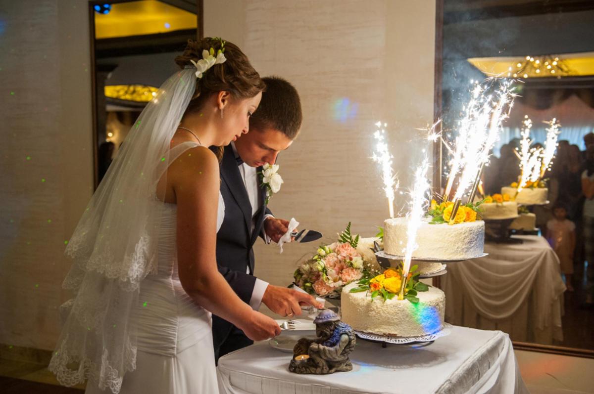 Para młoda kroi tort weselny z fontannami iskier, obok bukiet i figurka gnoma.
