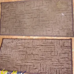 Dwa brązowe dywany z geometrycznym wzorem, ułożone jeden nad drugim na drewnianej podłodze; górny dywan z widocznymi plamami, dolny dywan z logo firmy czyszczącej w lewym dolnym rogu.